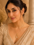 A woman wearing a delicate gold teardrop pendant necklace with small white pearl accents, styled with a beige embroidered blouse against a warm, elegant background.
